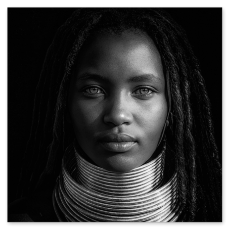 Schwarz-Weiß-Nahaufnahme einer afrikanischen Frau mit langen Haaren, die einen breiten, mehrlagigen metallischen Halsring und traditionelle Perlenketten vor einem dunklen Hintergrund trägt.